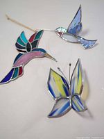 Three stained glass suncatchers showing butterfly and two hummingbirds