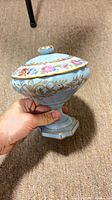 overall view of light blue porcelain covered compote showing floral lid band, gold gilt scrolls and pedestal base