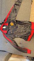 Full view of black and red Manchester United track jacket laid flat showing crest, zipper, cuffs and waistband