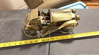 Side view of brass-tone model car with measuring tape for scale