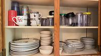 Cabinet view showing stacked stoneware plates, bowls, mugs, plastic tumblers, pitchers, glass bowl