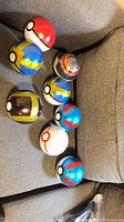 Eight assorted Poké Ball replicas displayed on grey sofa