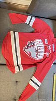 Front view of red Guelph Storm jersey showing crest, lace-up collar, stripes