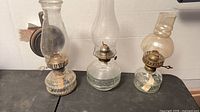 Front view of three glass kerosene lamps showing sizes, bases, burners and one wall bracket