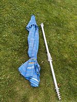 Umbrella canopy closed, aluminum pole and ground screw anchor laid out on grass