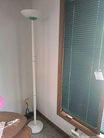 Full view of white metal torchiere floor lamp standing in corner showing pole, base, cord