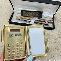 Open calculator notepad holder beside presentation box containing two pens