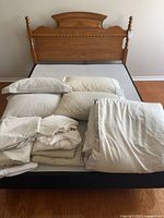 Queen bed showing wooden headboard, box spring, stacked pillows and folded bedding