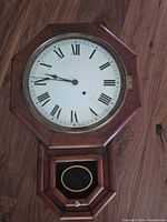 Front view showing octagonal clock face with Roman numerals and wooden case