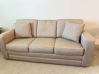 Front view of beige/tan three-seat sofa with cushions and pillows