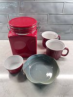 group shot showing all five items: red canister, two red mugs, red ramekin, teal bowl