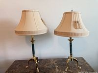 Pair of brass table lamps with green marble columns and beige shades displayed on tabletop