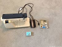 Singer sewing machine with foot pedal, accessory tray and ruffler box laid out on carpet
