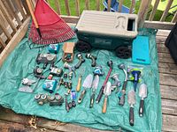 Full lot overview on tarp showing Lawn Buddy, rakes, timers, fittings, hand tools