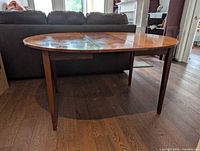 full view of round-to-oval teak dining table with leaf inserted and tapered legs