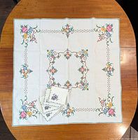 Full view of square tablecloth laid flat with napkins on top, shows overall design and set pieces