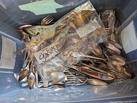 Overall view of bin filled with assorted flatware and serving pieces, labelled bag marked Sterling visible