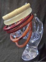 stack of six assorted bakelite bangles and one link bracelet on clear hand stand