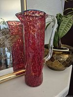 Full side view of red blown glass pitcher showing shape, handle, spout and color pattern