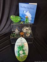 Overall group showing book, seven glass frog figurines, enamel frog, and packaged hook