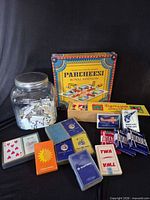 Group shot of Parcheesi box, jar of dominoes, wooden domino box, multiple playing card decks
