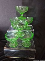 All six green ribbed pressed glass sherbet cups stacked on acrylic risers