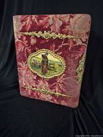 Front view of burgundy velvet photo album showing gilt trim and pastoral vignette