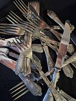 Pile of mixed ornate silver-plated forks and knives showing overall quantity and style