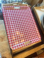 Red gingham tray on top of dark wooden tray and folding base, edge of black tray visible