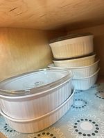 Stacked white fluted CorningWare casserole dishes with glass lids visible