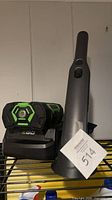 Shark handheld vacuum standing in cradle beside EGO battery in charger