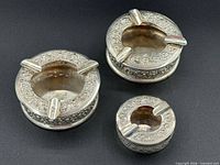 Top view of three ornate silver ashtrays showing size variation and decorative rims