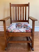 Front view of solid wood rocking chair showing slat back, arms, and floral cushion