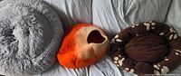 Overview showing three cat beds: grey plush, orange felted cave, brown paw-print