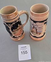 Front views of both steins showing relief scenes and size reference tag