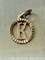 Front view of gold round charm with letter K and ridged border