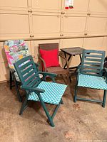Group view of three green resin chairs with cushions, brown wicker chair with pillow, wood side table, floral cushion