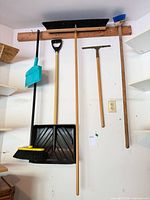 Full view of six long-handled tools hanging on wall