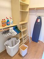 Closet view with ironing board, drying rack, hangers, cleaners, basket, waste bin