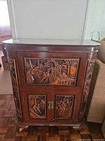 Front view of carved teak dry bar cabinet showing upper and lower doors with relief panels