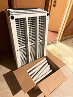 Front view of stacked plastic shelves leaning against wall with box of support poles