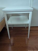 Front and side view of white wood side table showing lower shelf and tapered legs