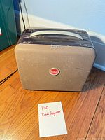 Brown Kodak-branded carrying case standing on hardwood floor with note reading "P30 8mm Projector"