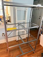 Full view of gray metal Origami shelving unit showing four wire shelves and casters