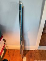 Folded teal metal projection screen with tripod stand leaning against wall