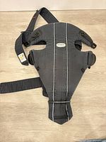 Full view of gray BabyBjörn Original carrier laid flat showing straps and buckles