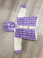Full view of white and purple striped crochet hooded cardigan laid flat