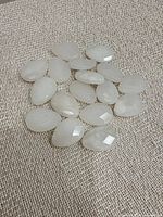 Group of 17 white translucent faceted teardrop cabochons on fabric background