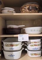 Cabinet view showing multiple CorningWare casseroles, amber baker, clear casserole in rattan basket