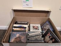 Open cardboard box filled with assorted music CDs
